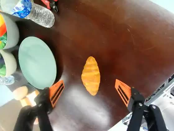 Wrist camera looking down between the gripper fingers at a croissant, with an empty pale-green plate to its left.