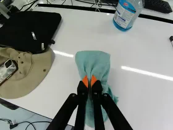 Wrist camera: the gripper holds a folded teal towel flat against a white desktop, a blue spray bottle beyond it.