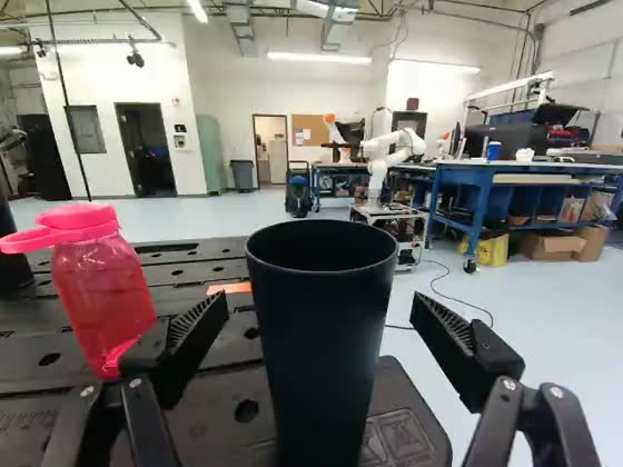 Wrist camera: the gripper is positioned over a dark cup and a pink bottle standing on a black workbench.