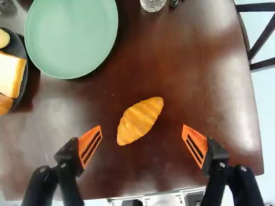 Wrist camera: the gripper is centred over a croissant on a dark wooden table, an empty green plate beside it.